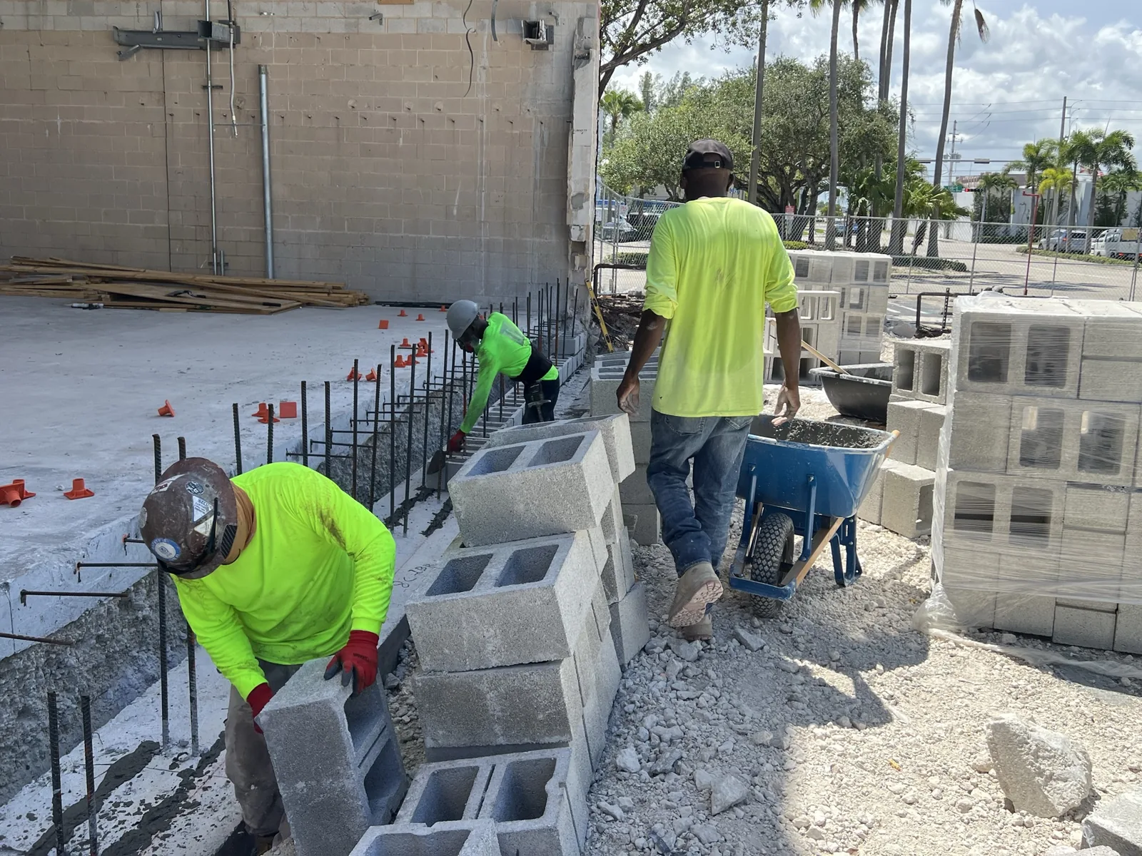 Mason laying the first course of block in mortar over a footing with dowels standing