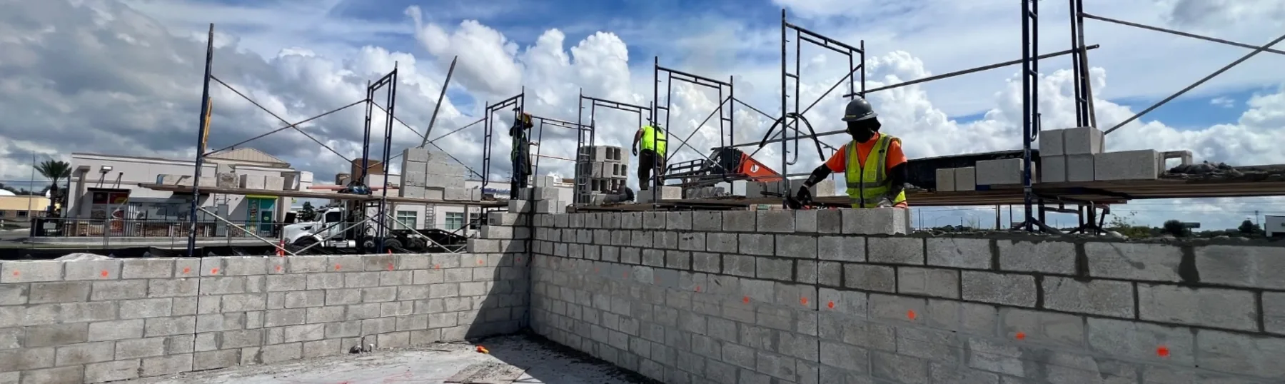 Masons in hard hats and hi-vis running a commercial CMU wall up to scaffold height