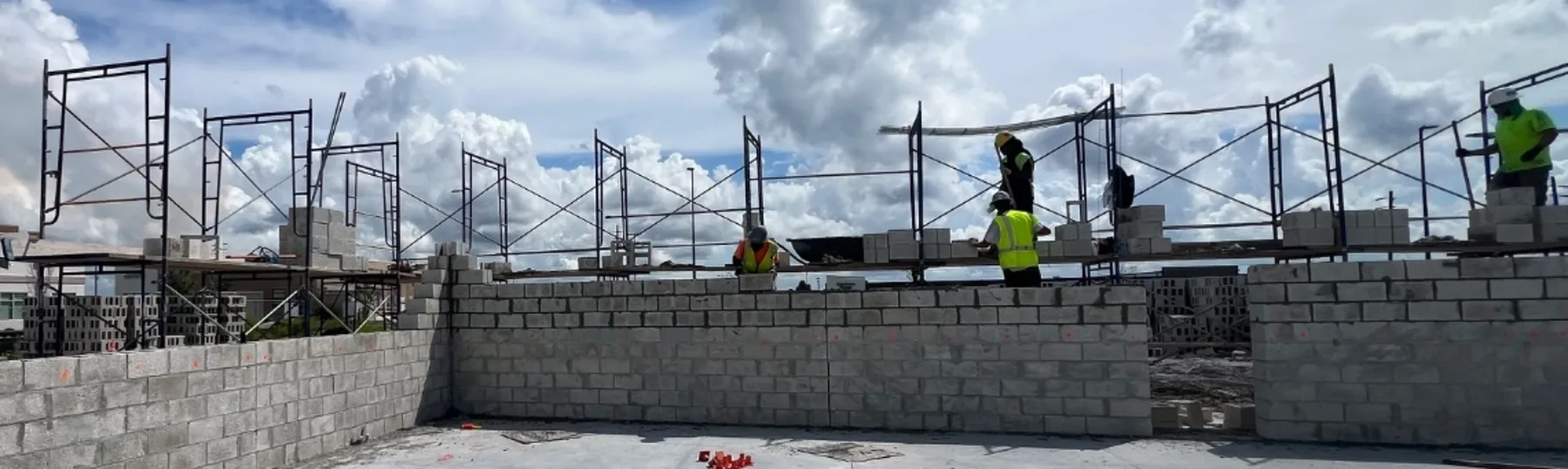 Concrete block walls run up around a finished slab on a commercial building, scaffolding staged the length of the wall and masons working the top course