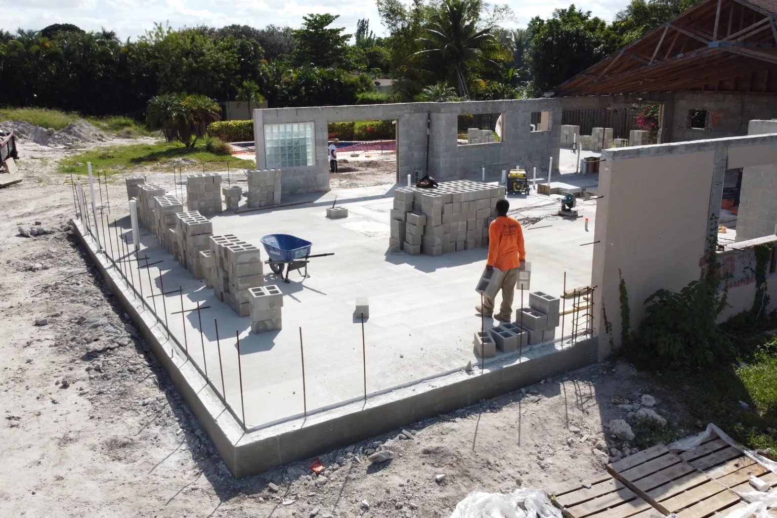 Mason carrying block across a finished slab beside stacked pallets