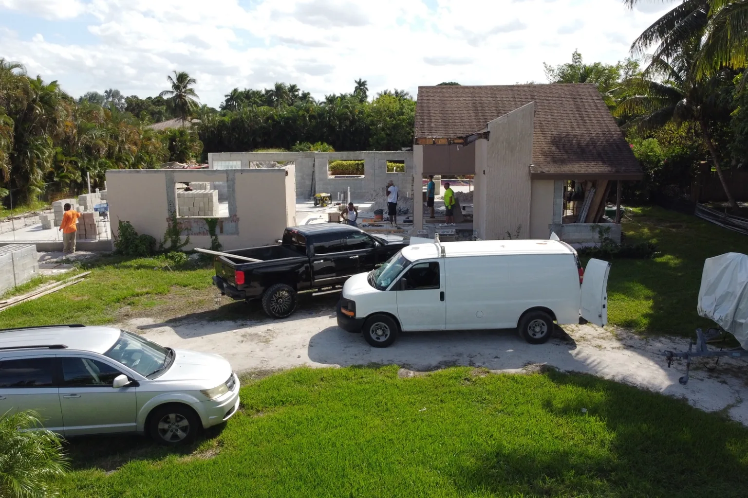 Aerial view of a residential jobsite with block walls up and crew trucks staged along the drive