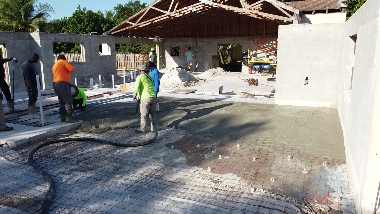 Crew placing concrete by pump hose over reinforcing mesh inside new block walls