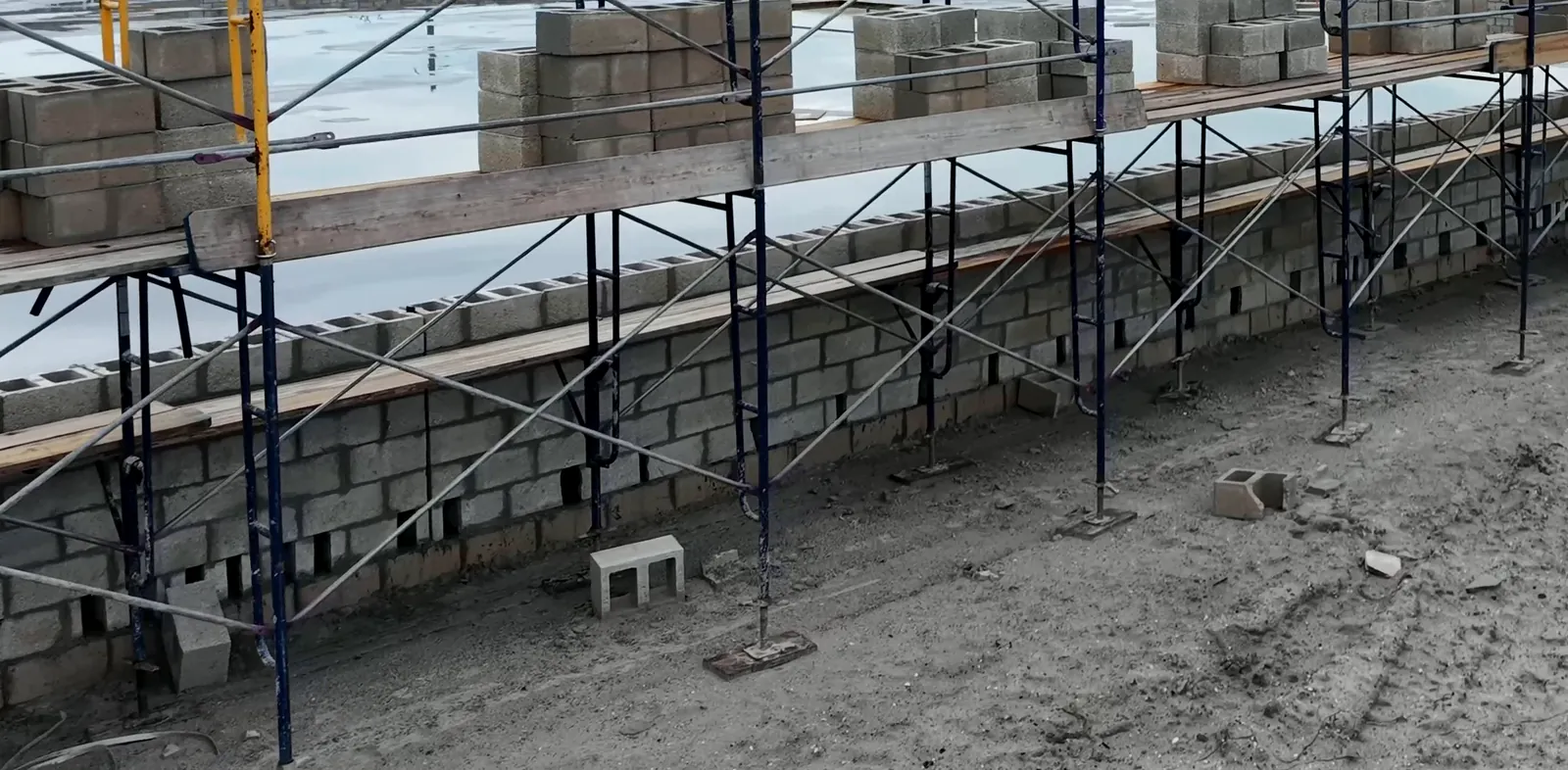 Aerial view along the full length of a commercial concrete block wall, scaffold set end to end and block staged on the planks